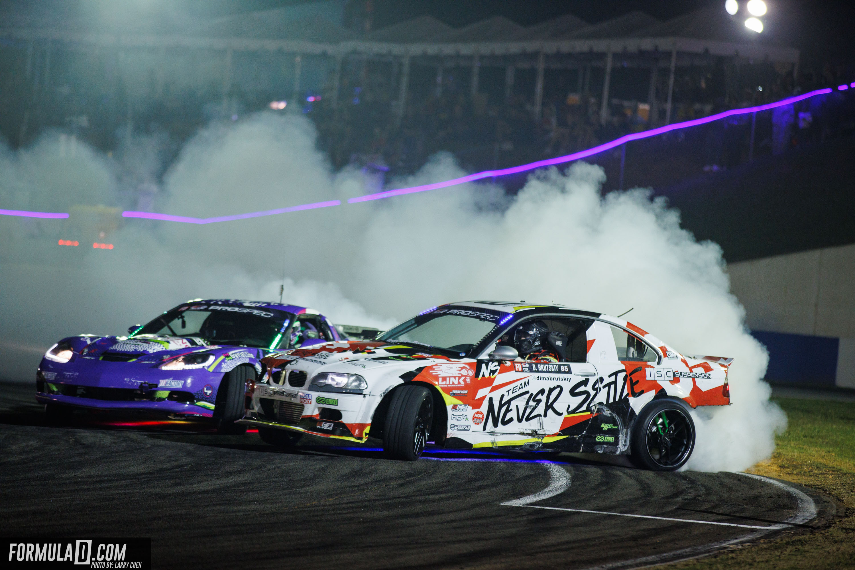 Formula Drift driver on track mid-drift with tire smoke trailing behind.