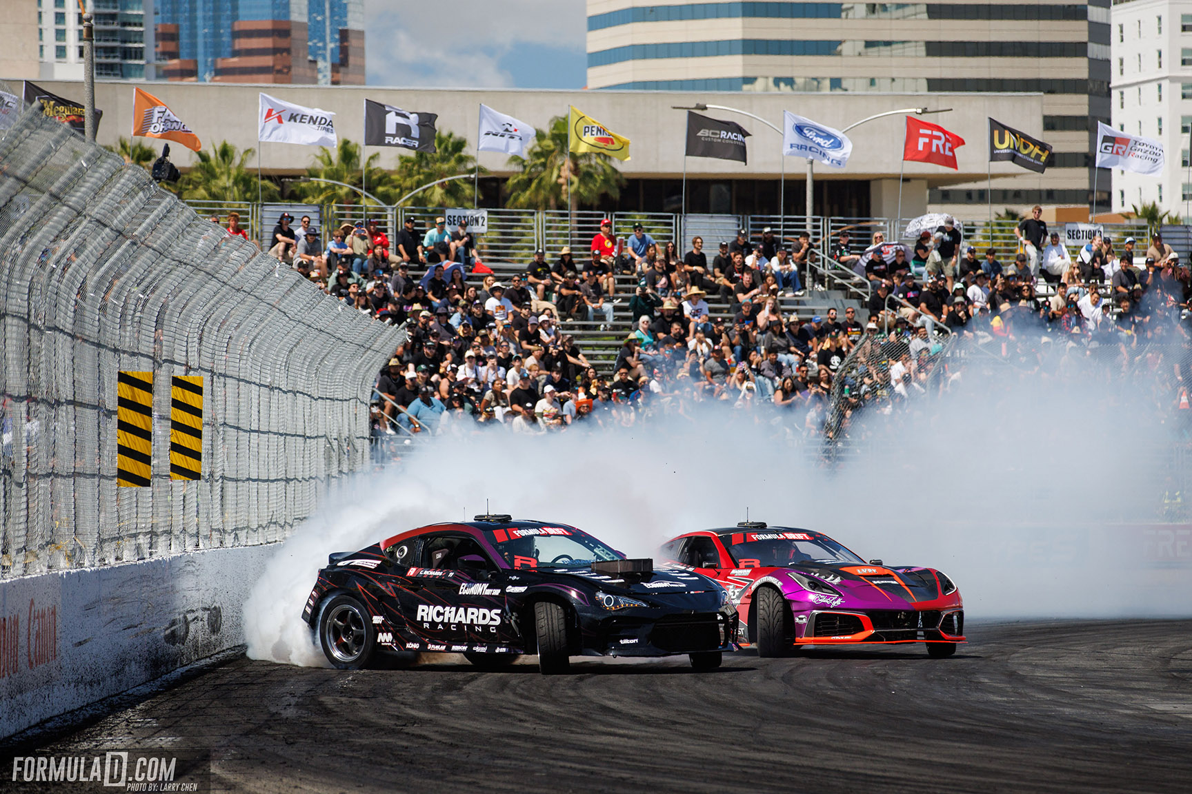Two drift cars battle through a smoke-filled corner in front of a packed crowd at Long Beach.