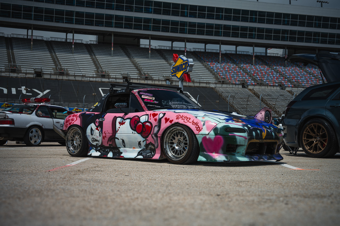 Custom Mazda Miata with a colorful anime-inspired livery displayed inside the FuelFest Dallas-Fort Worth show field at Texas Motor Speedway.