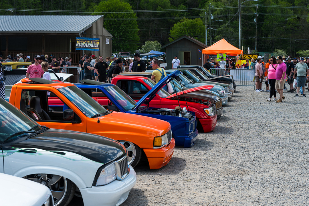 Custom mini trucks lined up at Mini Truckin’ Nationals with spectators and vendor booths in the background.