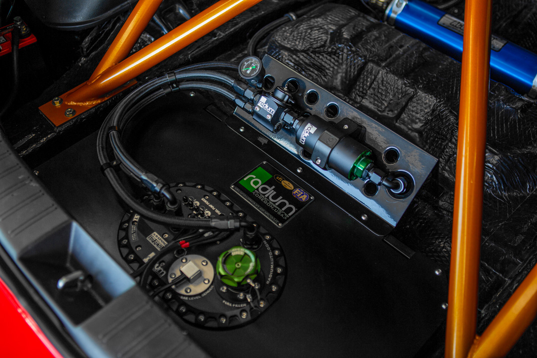 Close-up of the Radium fuel cell setup in Jon Erickson’s 2011 Subaru STi, shown with fuel lines, pressure gauge, and orange half cage.