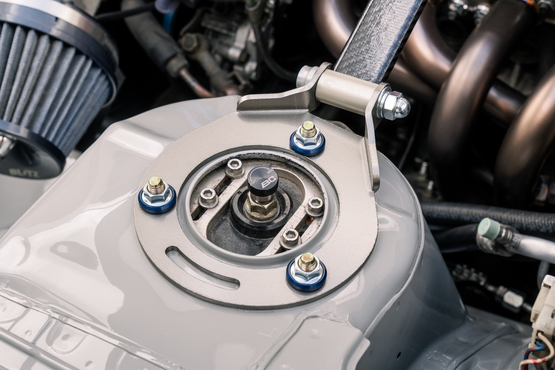 Close-up of Bill MacKenzie’s 2000 Nissan Silvia S15 showing the front strut tower, BC Racing coilover adjustment, Cusco strut bar, intake filter, and clean engine bay details.