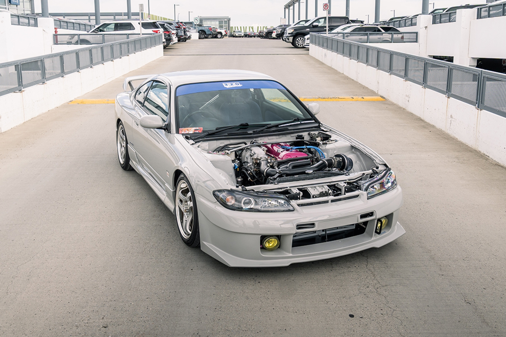 Bill MacKenzie’s Porsche Chalk 2000 Nissan Silvia S15 shown in a parking garage with Nismo aero, Super Advan V2 wheels, and exposed engine bay.