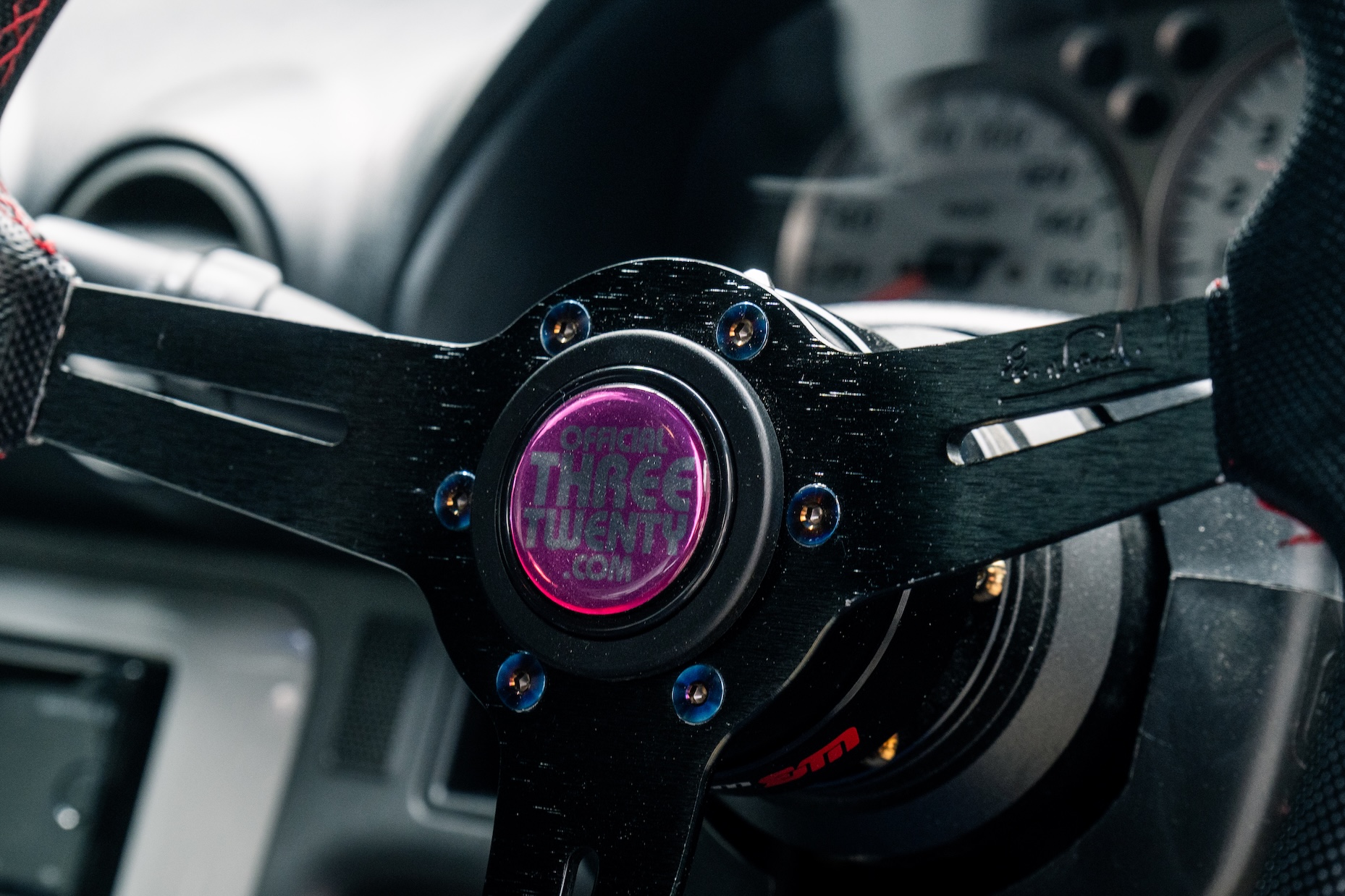 Close-up of Bill MacKenzie’s 2000 Nissan Silvia S15 interior showing the steering wheel, officialTHREETWENTY horn button, quick-release hub, and gauge cluster.