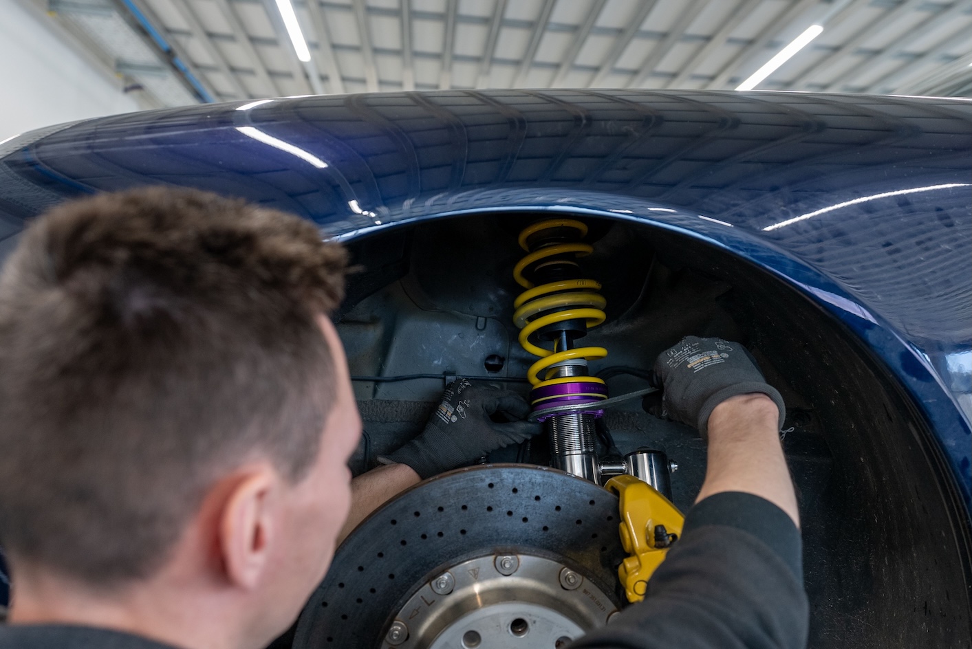 Technician installing a KW DDC Plug & Play coilover on a Porsche 911 997 with the front wheel removed.