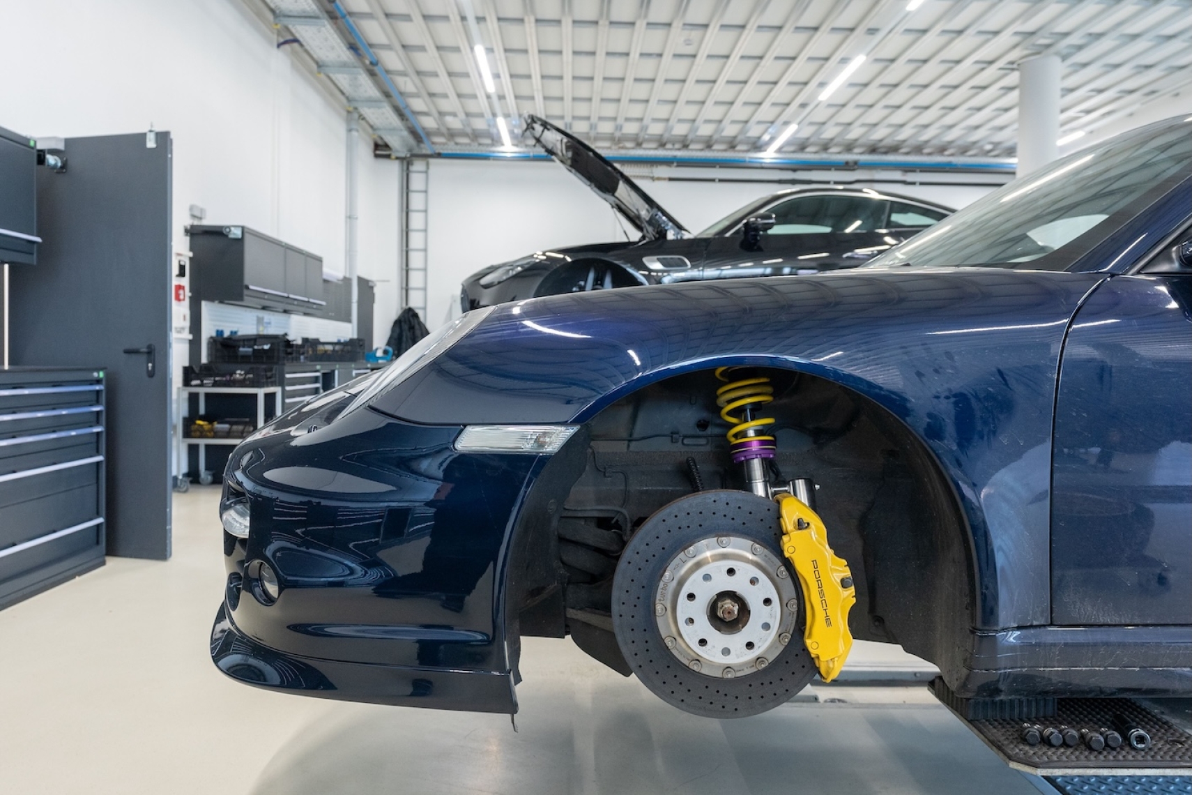 KW DDC Plug &amp; Play coilover installed on a Porsche 911 997 with the front wheel removed inside a workshop.