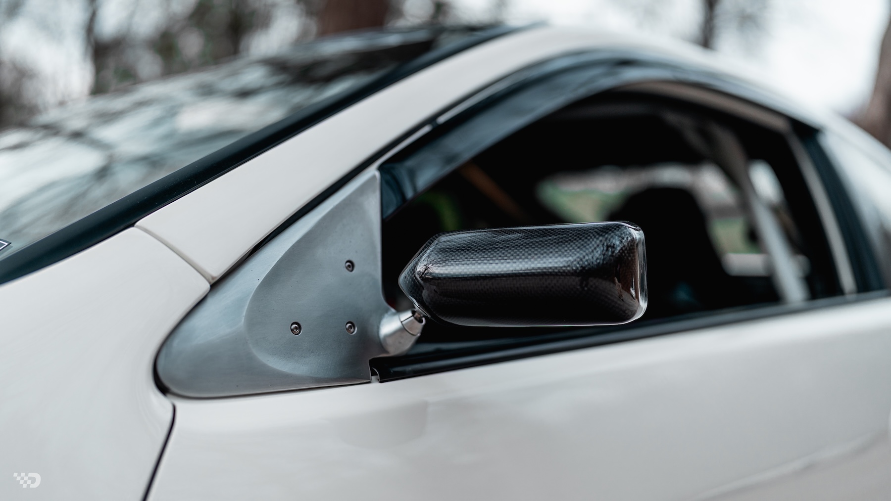 Close-up of Moises Wynns’ 2003 Acura RSX showing the Craft Square carbon side mirror, custom mounting plate, and right-hand-drive cabin detail.