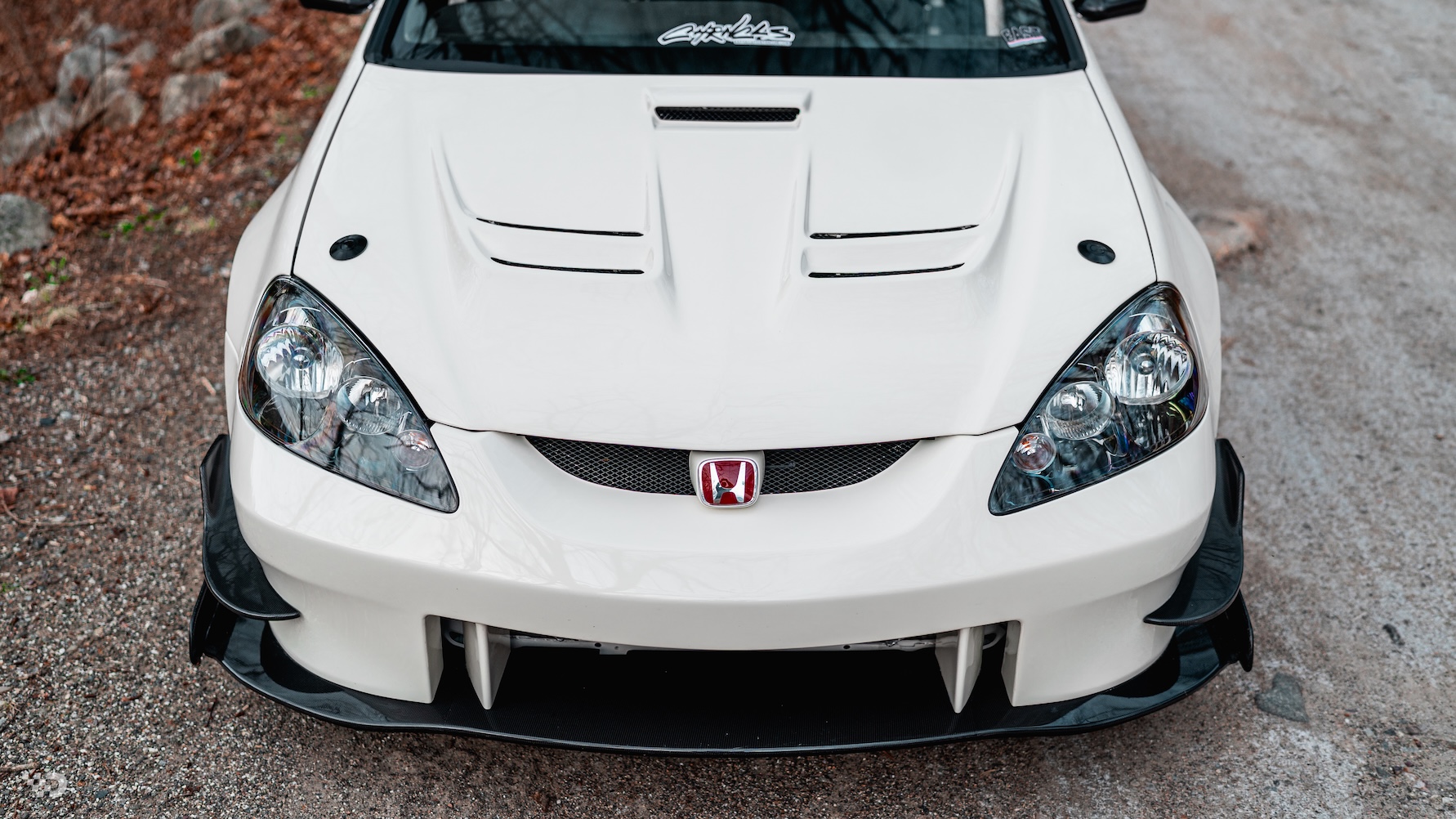 Front-end detail of Moises Wynns’ Championship White 2003 Acura RSX showing the J’s Racing hood, front bumper, splitter, headlights, and red Honda badge.