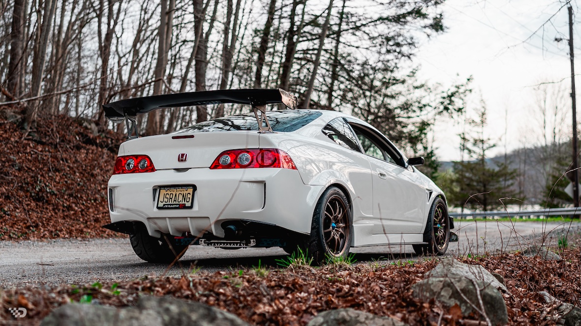 Rear three-quarter view of Moises Wynns’ Championship White 2003 Acura RSX showing the J’s Racing rear bumper, large rear wing, Mugen MF10 wheels, and custom aero.