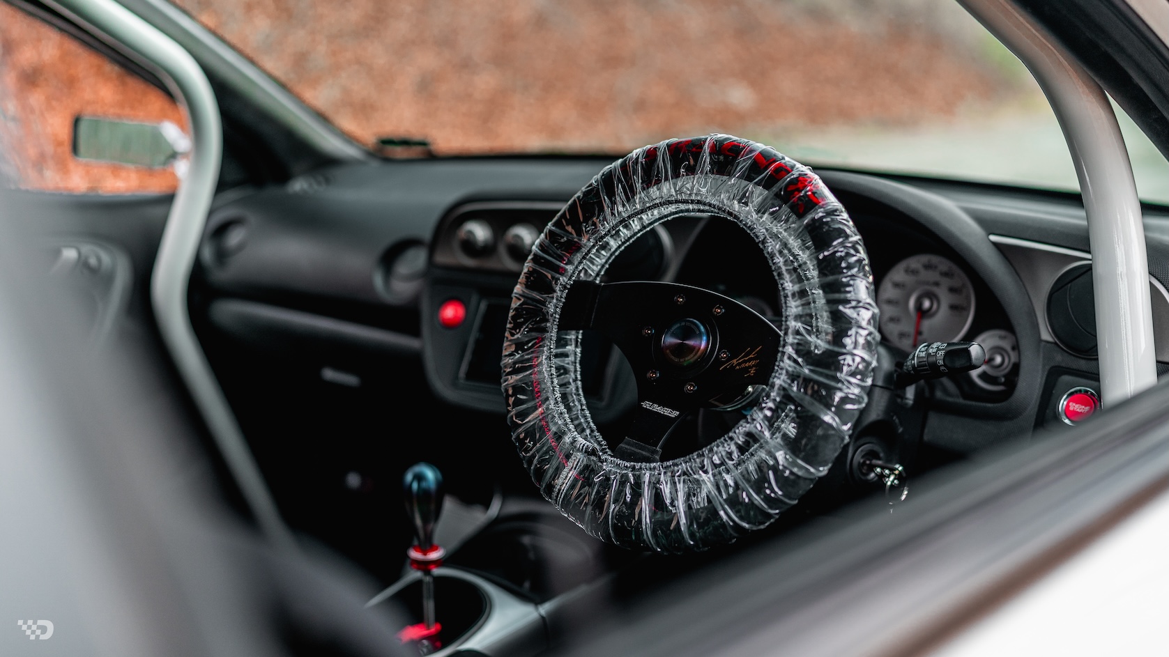 Interior detail of Moises Wynns’ right-hand-drive 2003 Acura RSX showing the J’s Racing signed steering wheel, shifter, roll cage, and DC5 Type R-style cockpit.