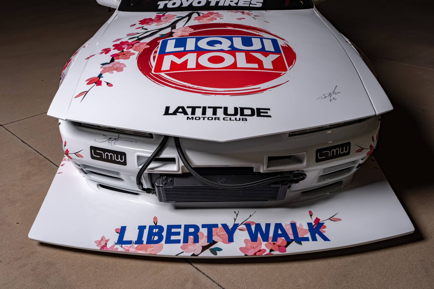 Front detail of Osmond Seangsuwan’s 1990 Nissan Skyline GT-R showing the LIQUI MOLY hood livery, Liberty Walk front aero, LTMW branding, Toyo Tires banner, and cherry blossom artwork.