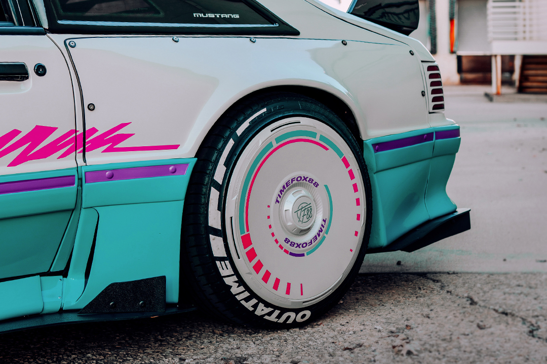 Close-up rear wheel detail of Regan McLaughlin’s 1988 Ford Mustang GT TimeFox showing the HaloBLK HaloDisc setup, custom wide fiberglass fender, teal and pink graphics, rear quarter aero, and retro Foxbody styling.