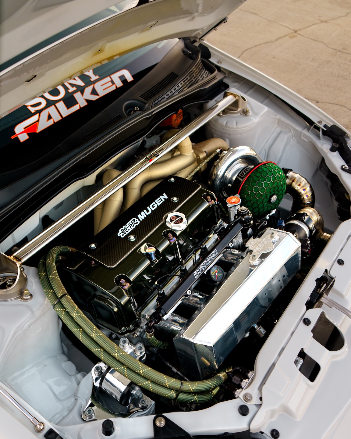 Engine bay detail of Jonathan Ortiz’s 2005 Acura RSX Type-S showing the turbocharged K-series setup, Mugen coil cover, BorgWarner turbo, titanium charge piping, K-Tuned fuel rail, and tucked radiator setup.