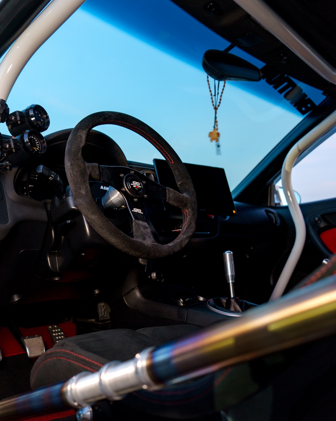 Driver cockpit detail of Jonathan Ortiz’s 2005 Acura RSX Type-S showing the Mugen steering wheel, ASM steering wheel hub, AEM gauges, shifter, Cusco cage, and titanium door bar.