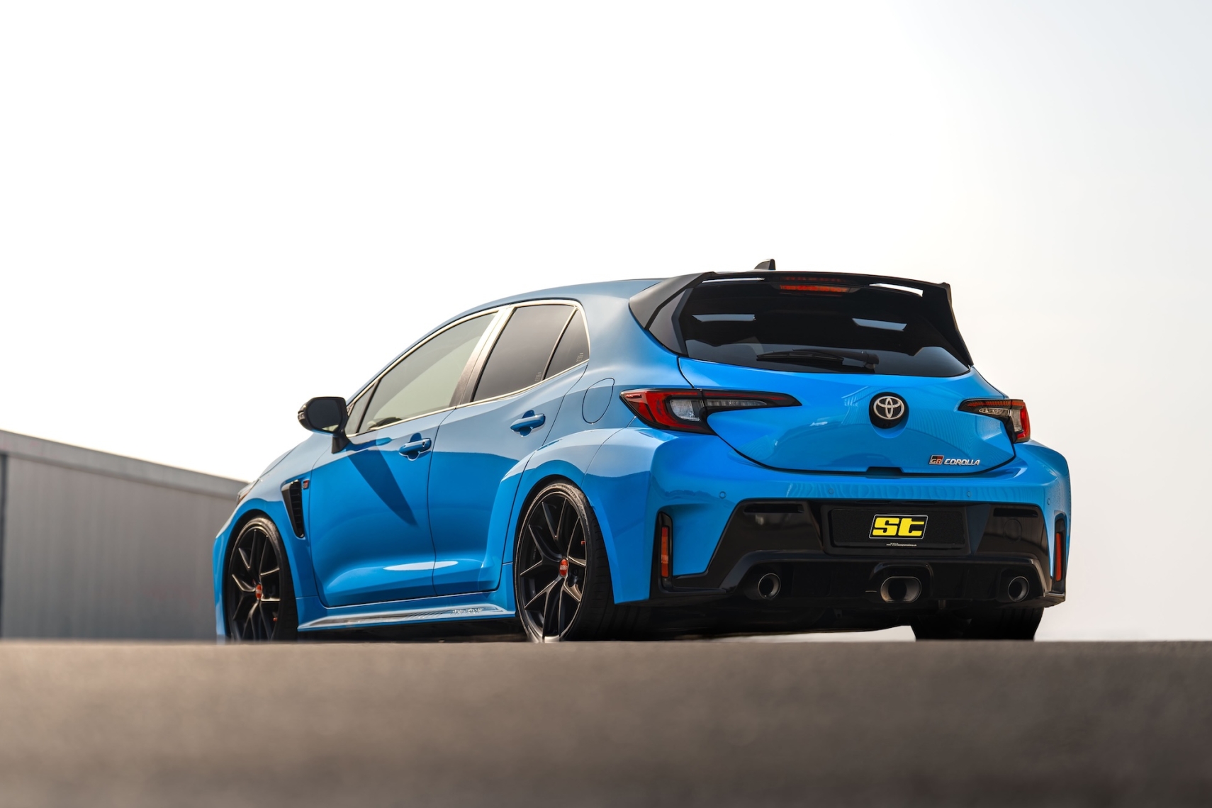 Blue Toyota GR Corolla equipped with ST XTA plus 3 coilover suspension shown from a low rear three-quarter angle.