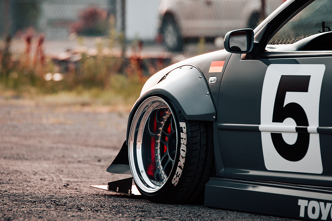 Close-up detail of a modified Toyota show build with wide fenders, polished wheels, Toyo tire lettering, aero, and race-style number graphics.
