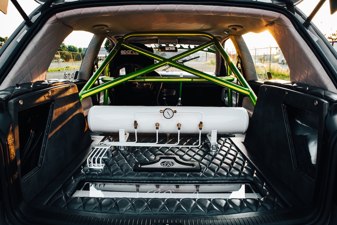Custom trunk setup with quilted upholstery, green roll cage, air tank, hard lines, and fabricated panels.