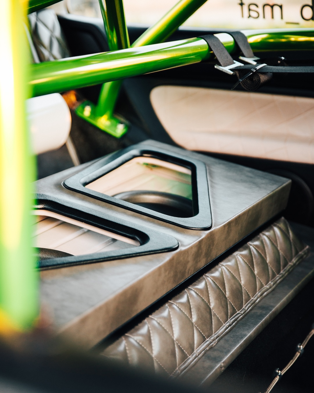 Custom interior detail with green roll cage, quilted upholstery, harness straps, and fabricated rear seat delete panel.
