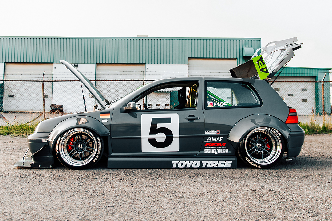 Side profile of a widebody Volkswagen Golf show build with custom fender flares, front splitter, deep wheels, and Toyo Tires graphics.