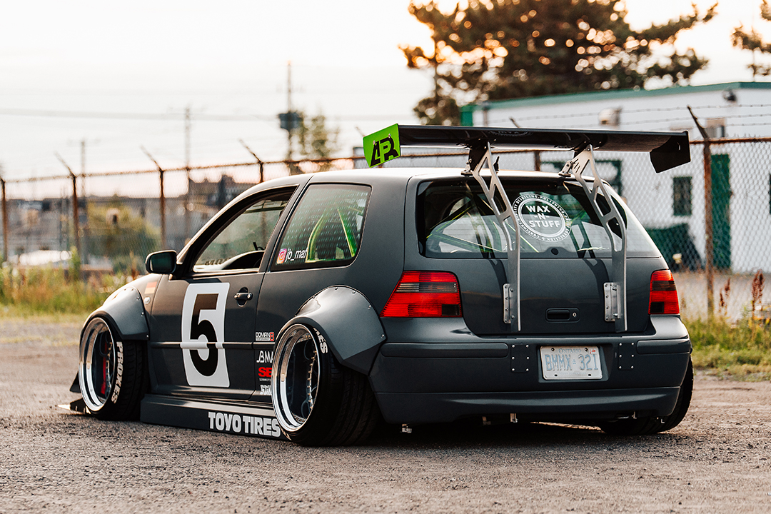 Rear three-quarter view of a widebody Volkswagen Golf show build with large rear wing, deep wheels, Toyo Tires graphics, and race-style number livery.