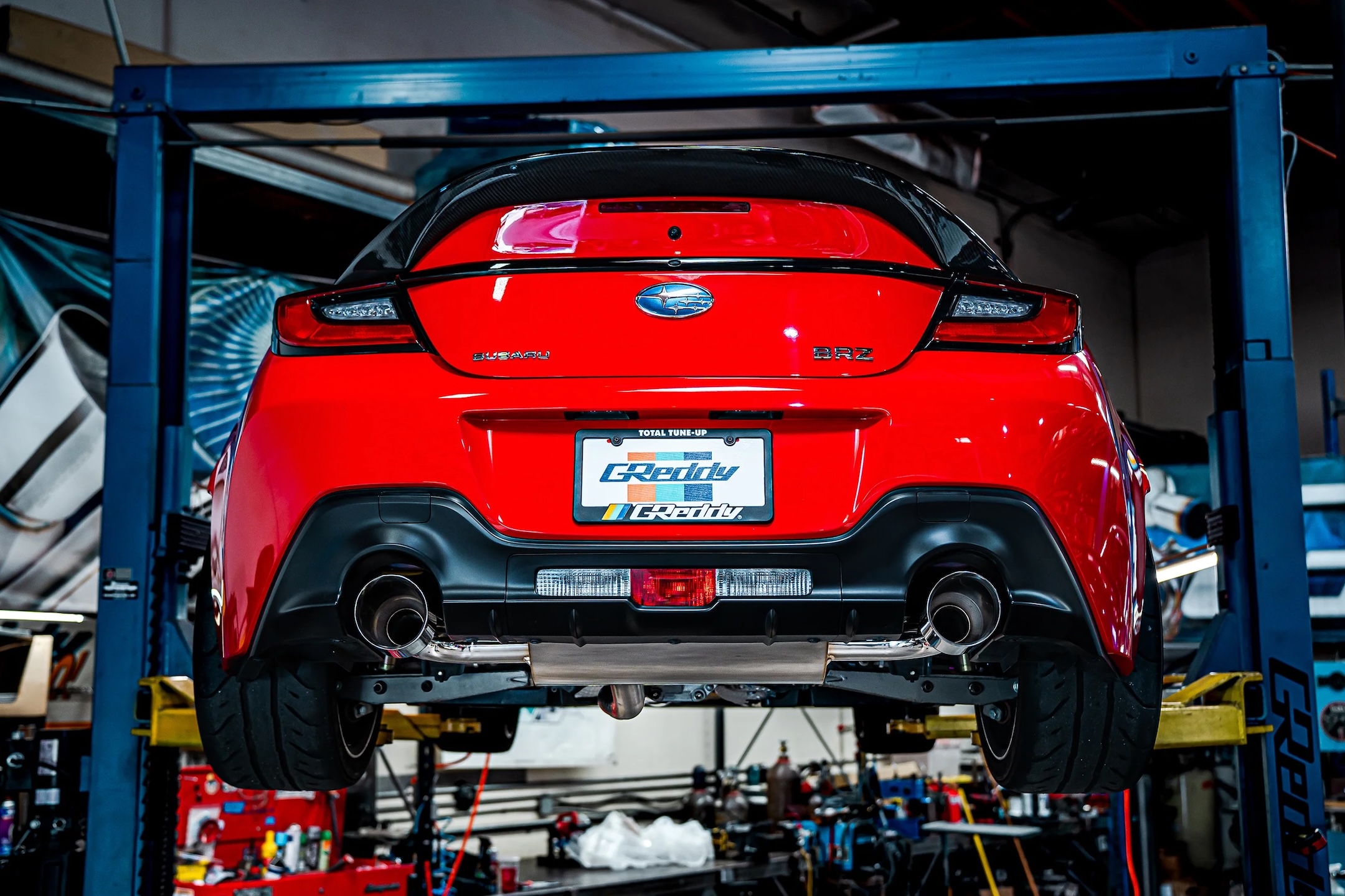 GReddy Supreme SP cat-back exhaust installed on a red Subaru BRZ with dual polished exhaust tips visible under the rear bumper.
