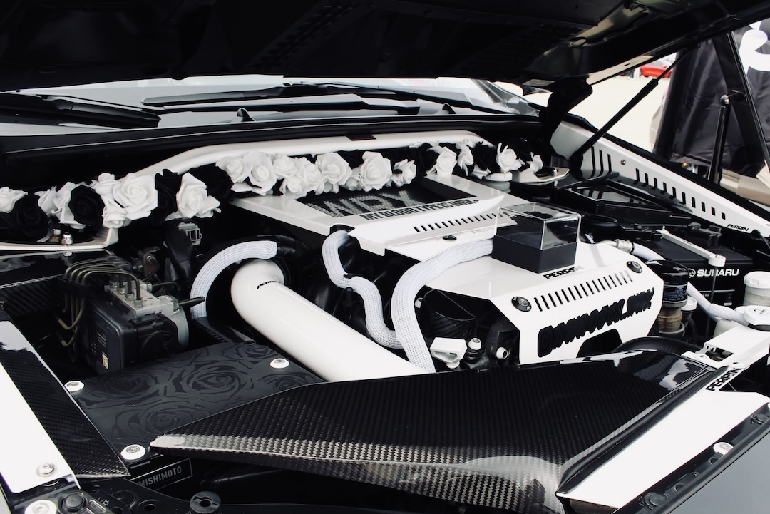 Engine bay detail of Melissa Pelletier’s 2017 Subaru WRX showing the black-and-white rose theme, carbon fiber accents, white engine bay dress-up components, Perrin details, and decorative rose accents.
