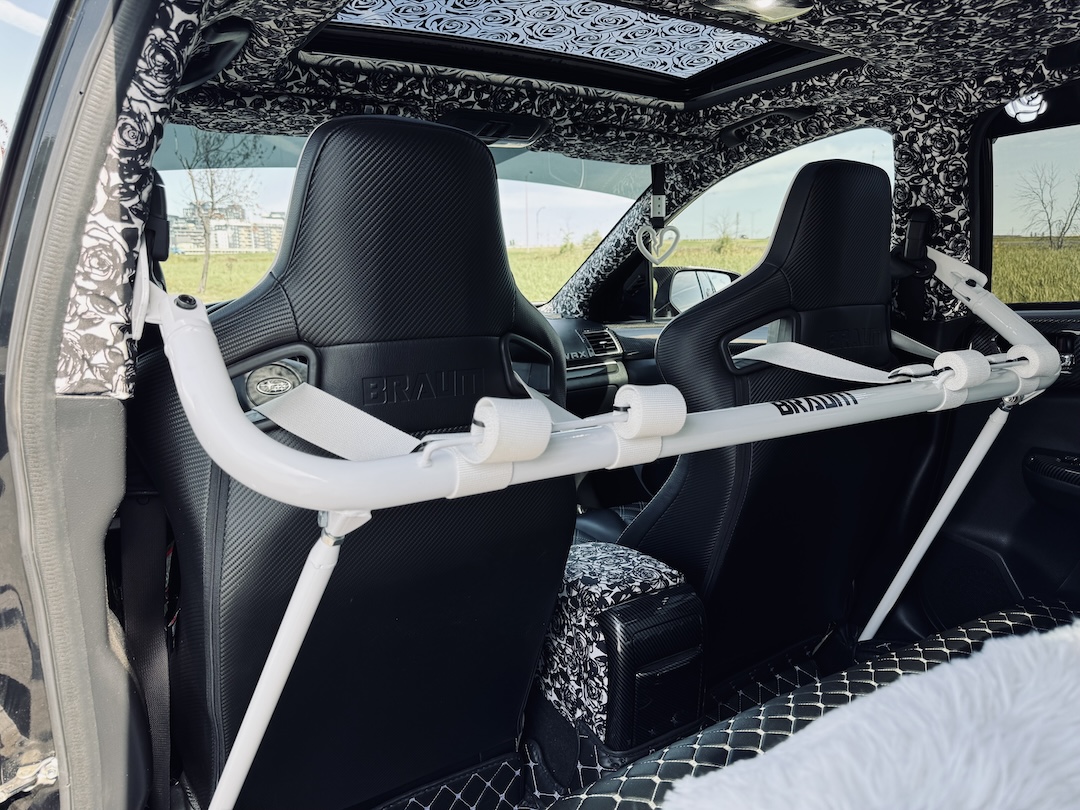 Rear cabin detail of Melissa Pelletier’s 2017 Subaru WRX showing the Braum Racing seats, white harness bar, rose-pattern headliner, custom upholstery, and black-and-white interior theme.