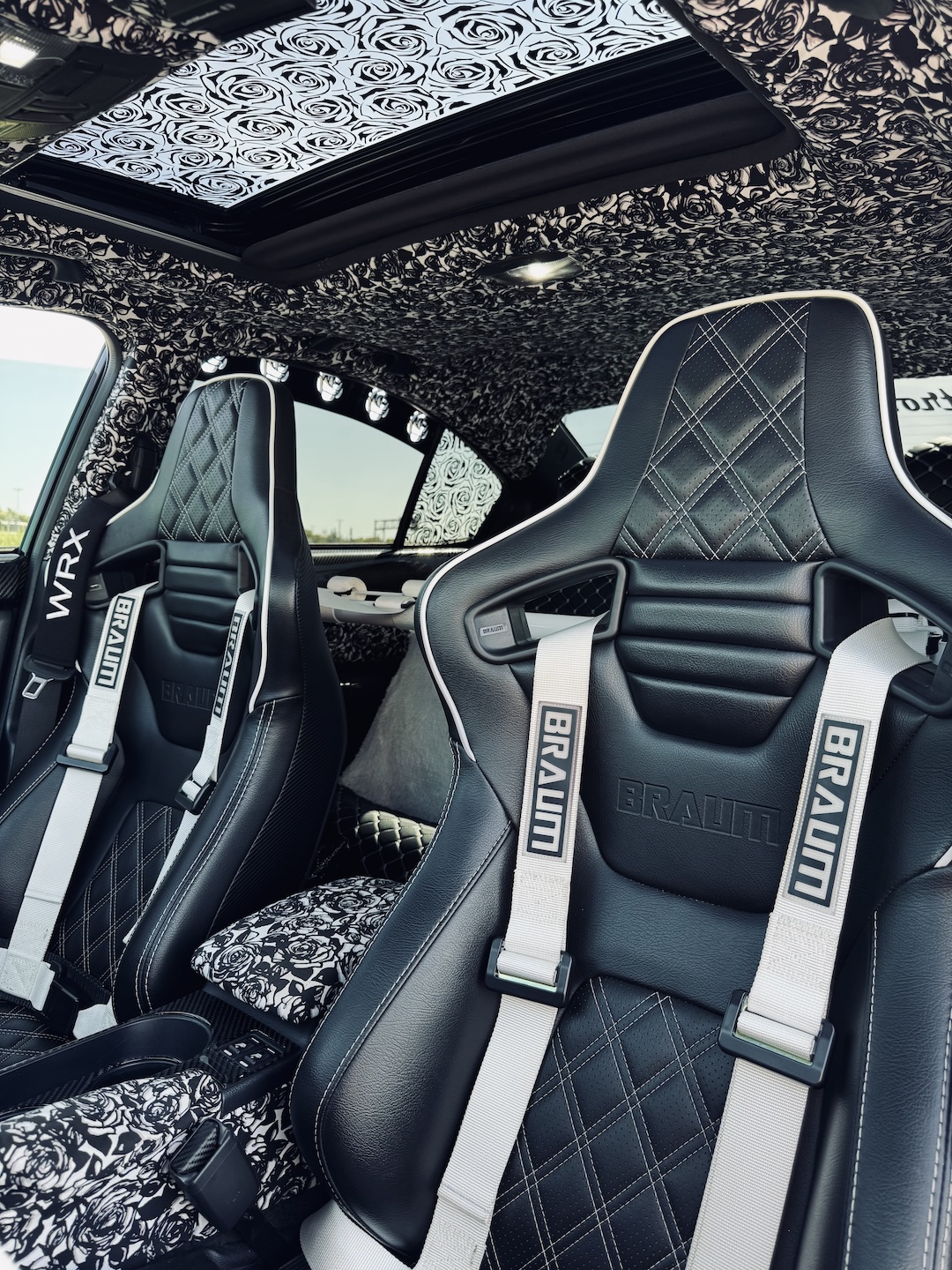 Interior detail of Melissa Pelletier’s 2017 Subaru WRX showing the black-and-white rose upholstery, Braum Racing seats, white harnesses, custom headliner, sunroof panel, and coordinated cabin theme.