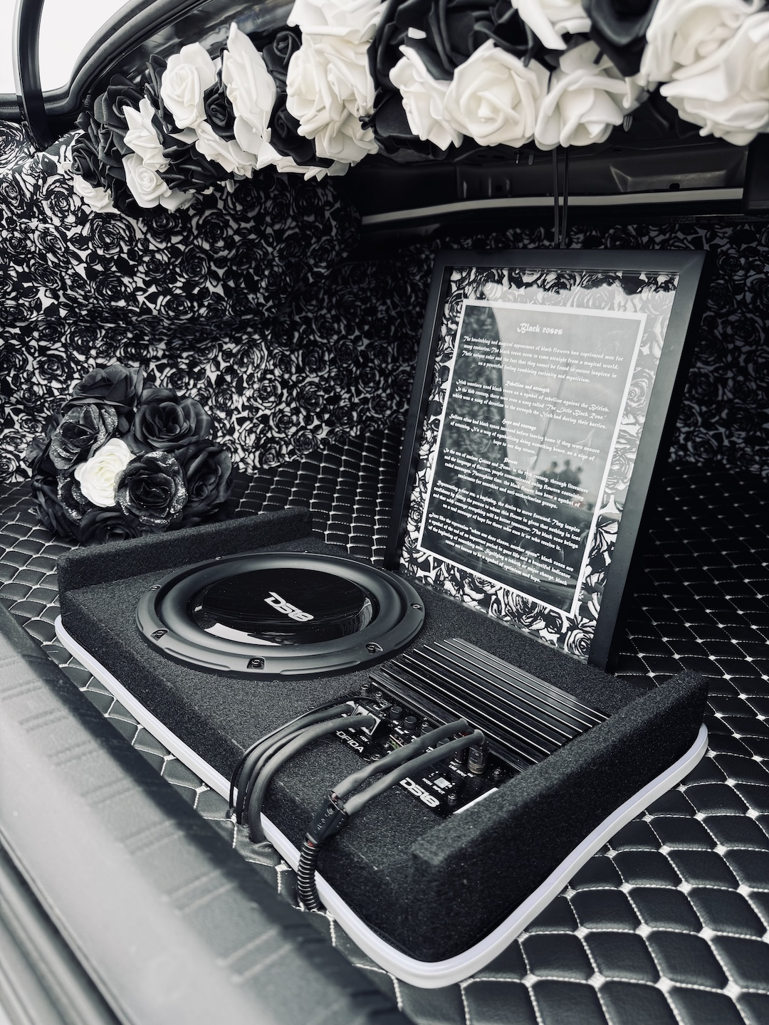 Trunk detail of Melissa Pelletier’s 2017 Subaru WRX showing the black-and-white rose upholstery, DS18 audio setup, subwoofer, amplifier, decorative roses, and custom display panel.
