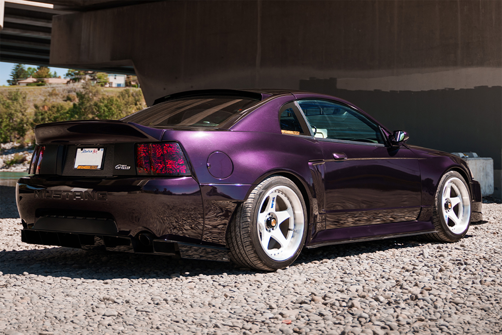 Rear three-quarter view of Jason Wang's 1999 Ford Mustang GT showing its Infamous Aero widebody, Nissan Midnight Purple paint, white INFMS LemonGT prototype wheels, and custom rose-patterned taillights.