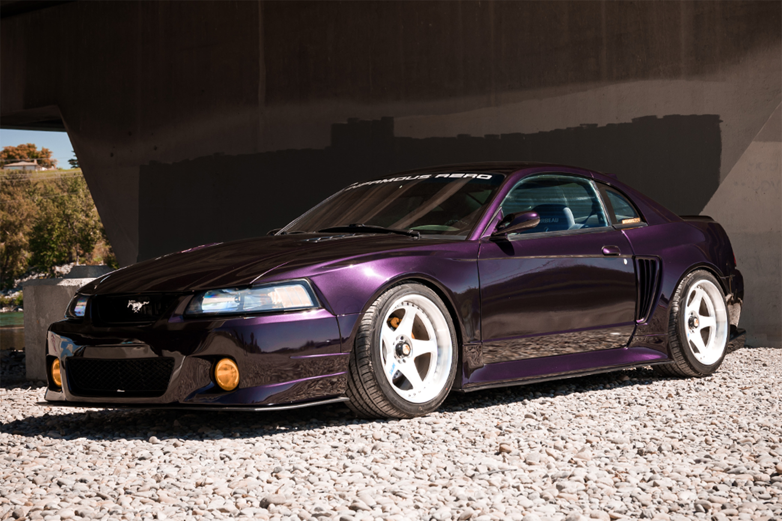 Front three-quarter view of Jason Wang's 1999 Ford Mustang GT featuring Nissan Midnight Purple paint, Infamous Aero widebody components, and white INFMS LemonGT prototype wheels.
