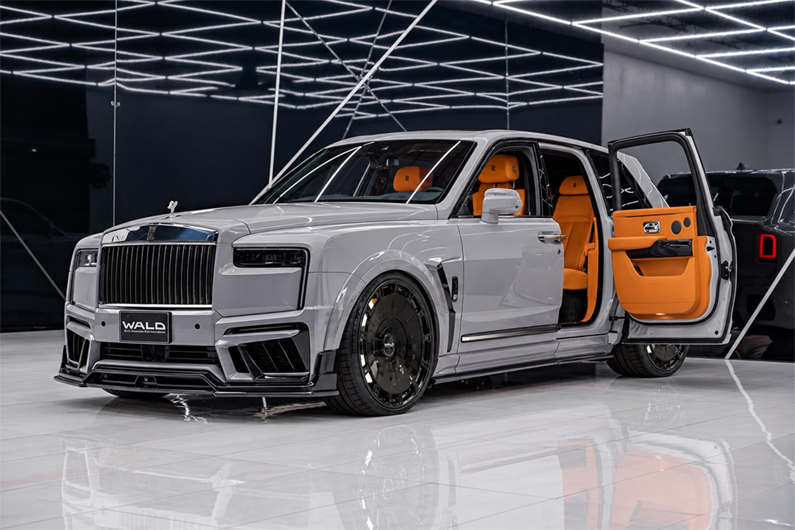 Front three-quarter view of the 2027 Rolls-Royce Cullinan by WALD USA, featuring the Black Bison body kit, gloss-black wheels, lowered suspension and bright orange leather interior.