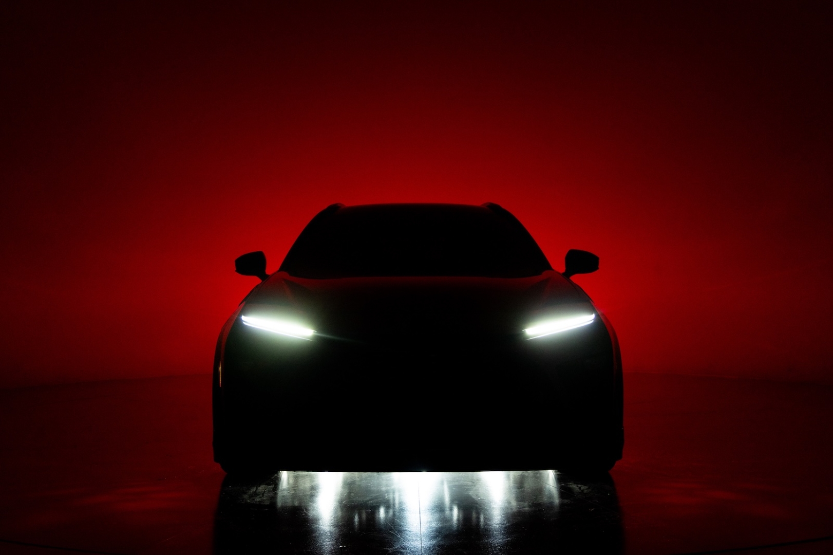 Front silhouette of the Toyota Crown Signia GT-S Concept against a dramatic red background, highlighting its illuminated LED headlights and aggressive stance.